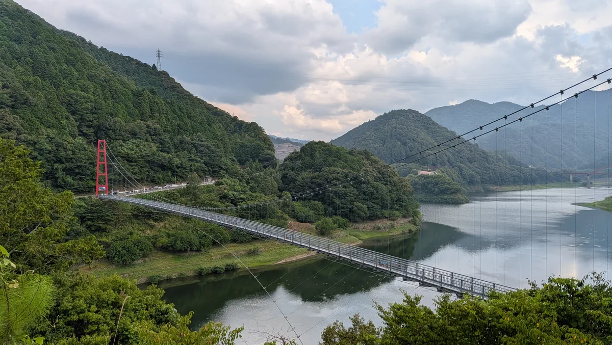 道中の椿山ダム湖に架かる赤い吊り橋・椿山レイクブリッジと山々の風景